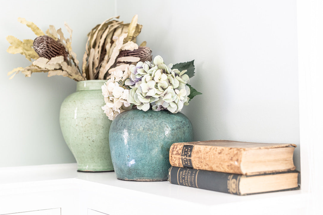 Two ceramic vases with flowers and books on a white surface