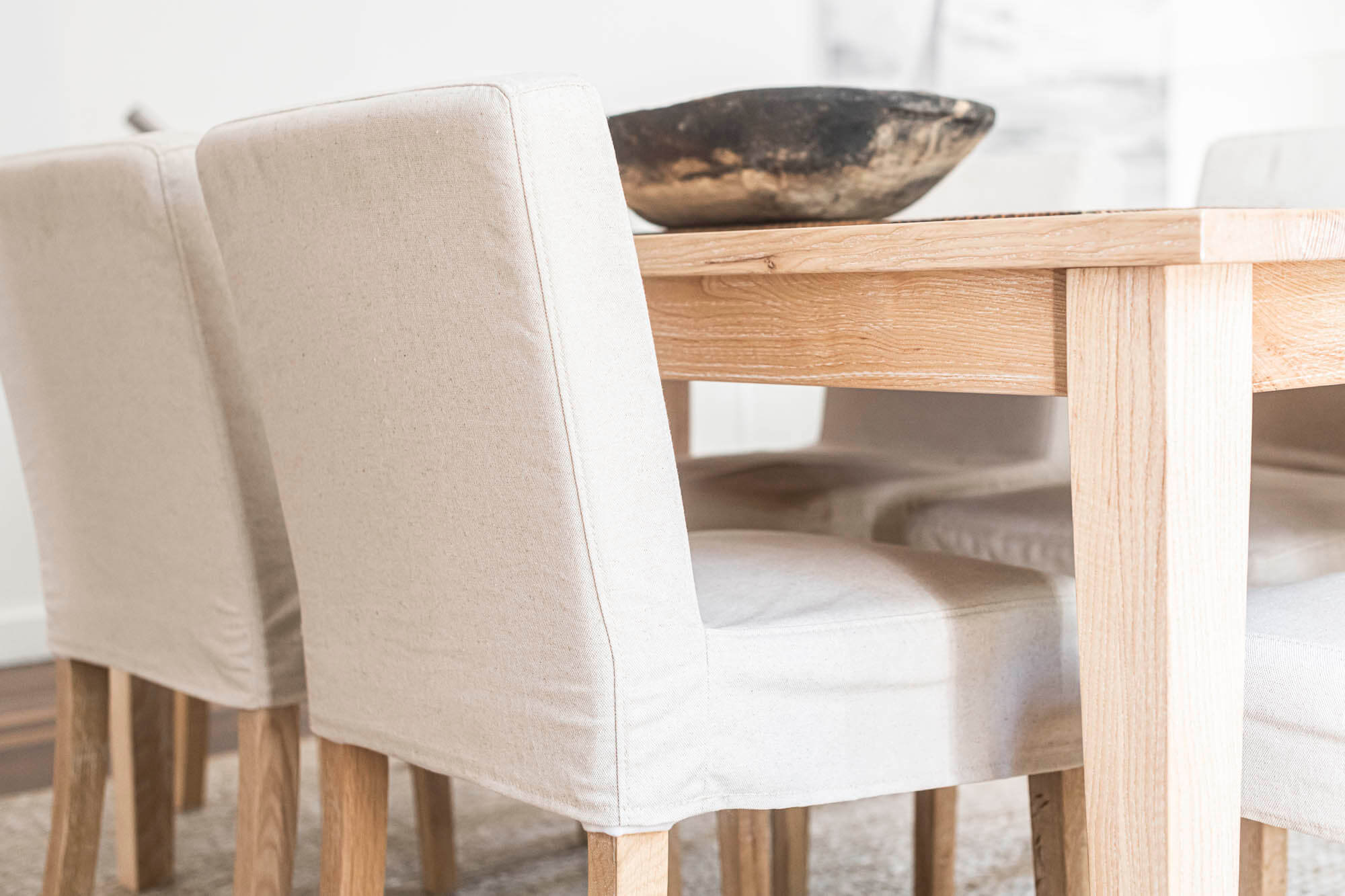 Wooden dining table with beige chairs and a decorative bowl on a light background