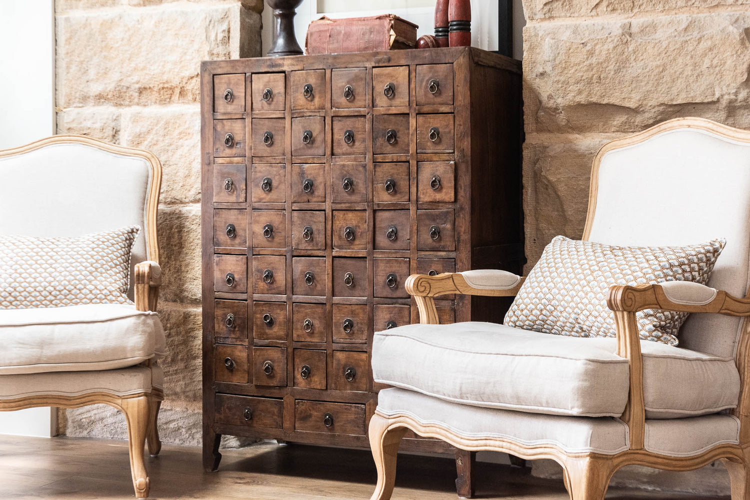 Wooden cabinet with drawers in a room with stone walls and white chairs.