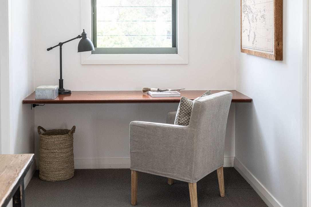 Small home office with a wooden desk, chair, and lamp in a room with a window.