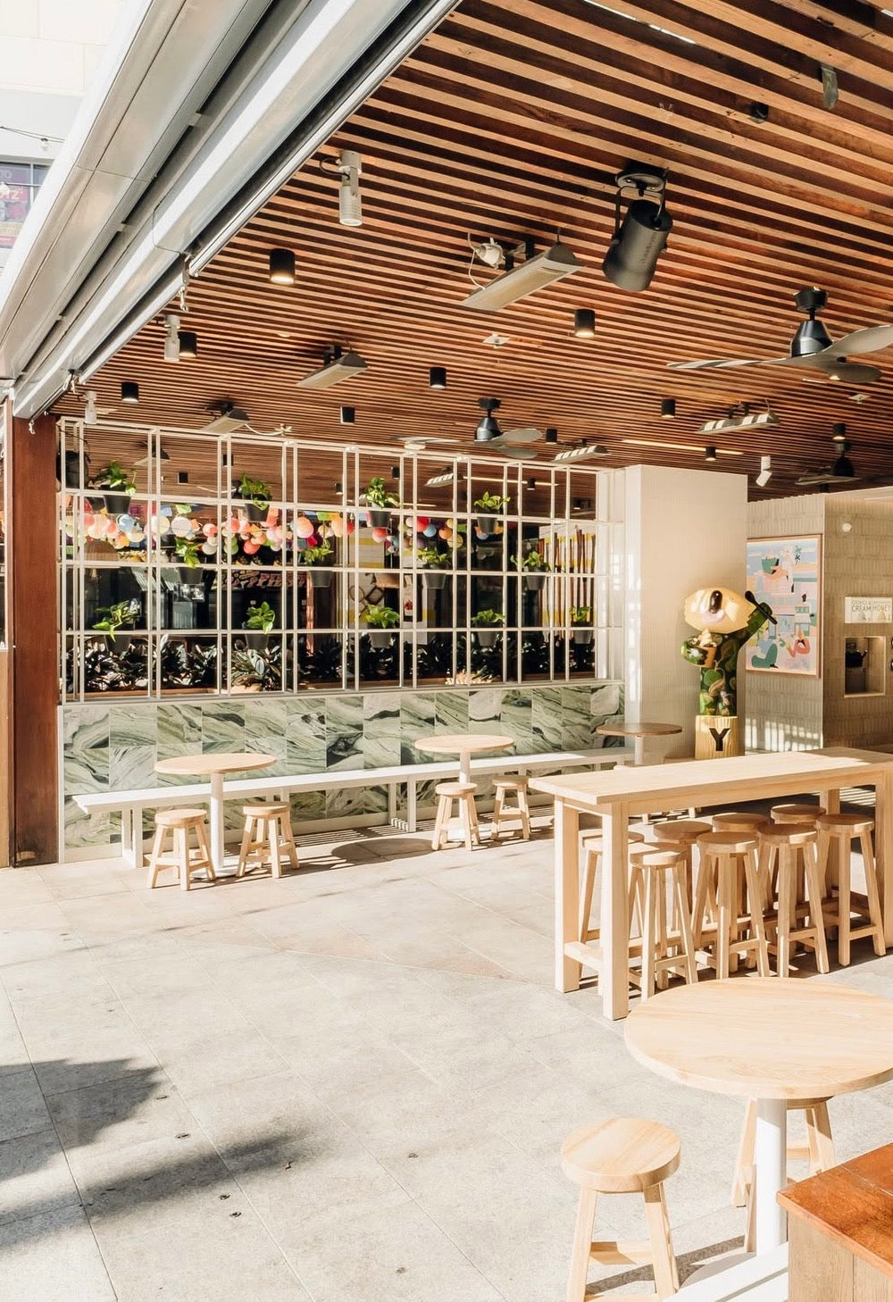 Modern interior of a cafe with wooden tables, stools, and decorative plants.