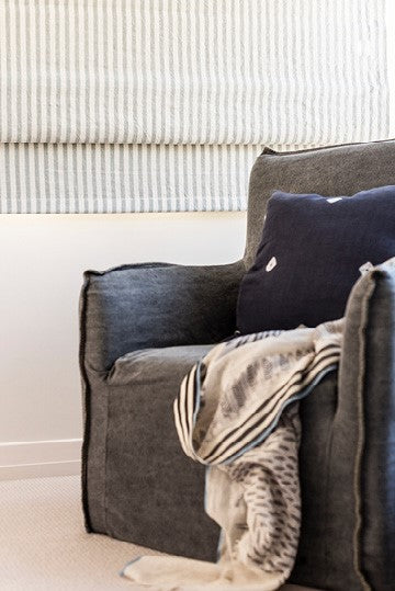 Cozy dark grey armchair with decorative navy blue pillow and throw blanket, with striped curtains in the background, perfect for modern home decor