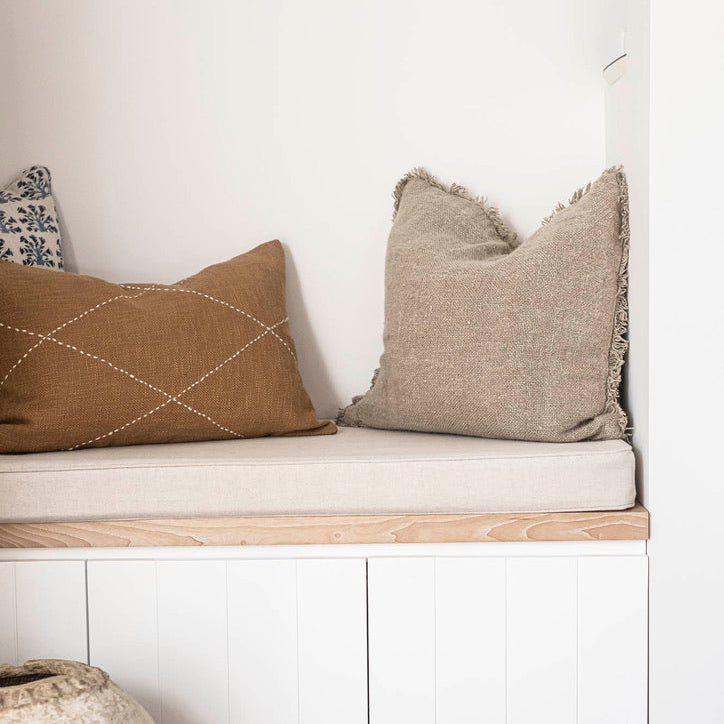 A built-in bench seat with a light wood top and white storage cabinet below, styled with two textured throw pillows in a bright room with a wood floor.