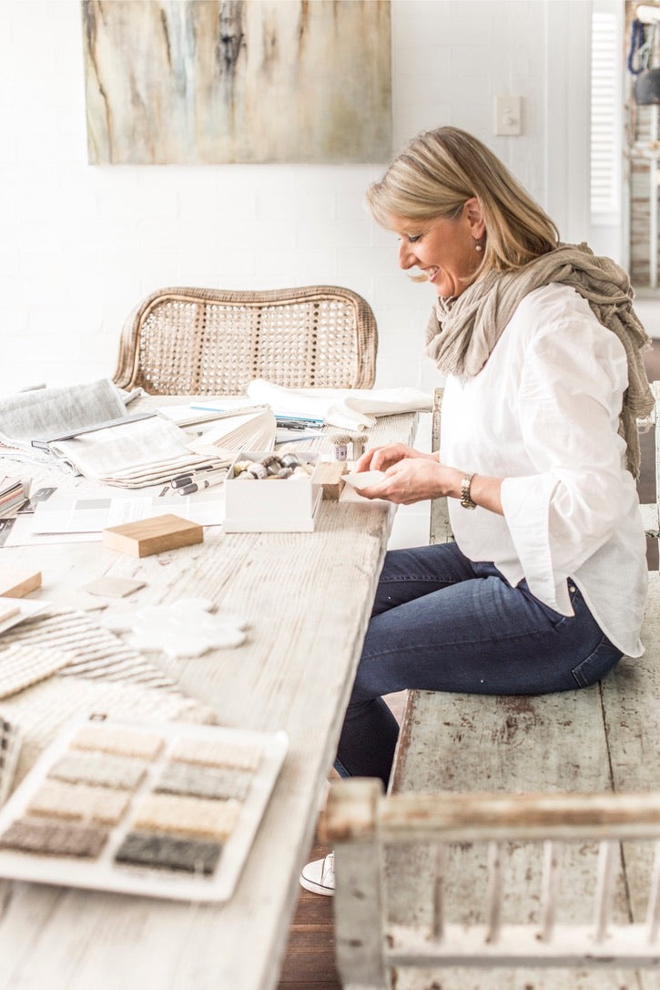 Woman sitting at a table with material samples, possibly in a design or home decor setting.