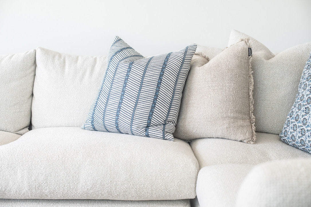A close-up of a light beige upholstered sofa with several decorative throw pillows, including a prominent blue and white striped pillow and neutral beige pillows.