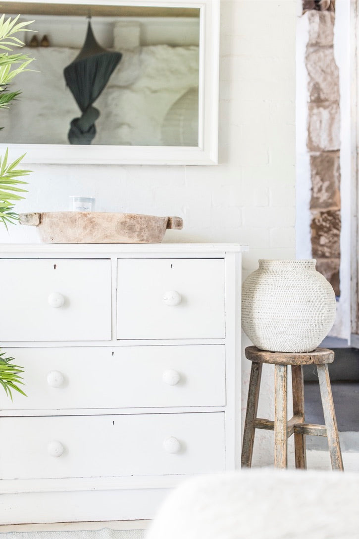 White dresser with decorative items including a plant, mirror, and spherical lamp in a room setting.