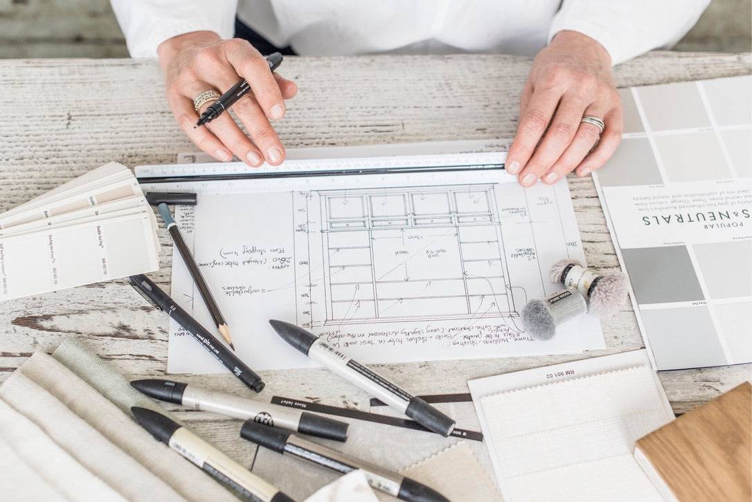 Person working on furniture blueprints with tools and documents on a desk