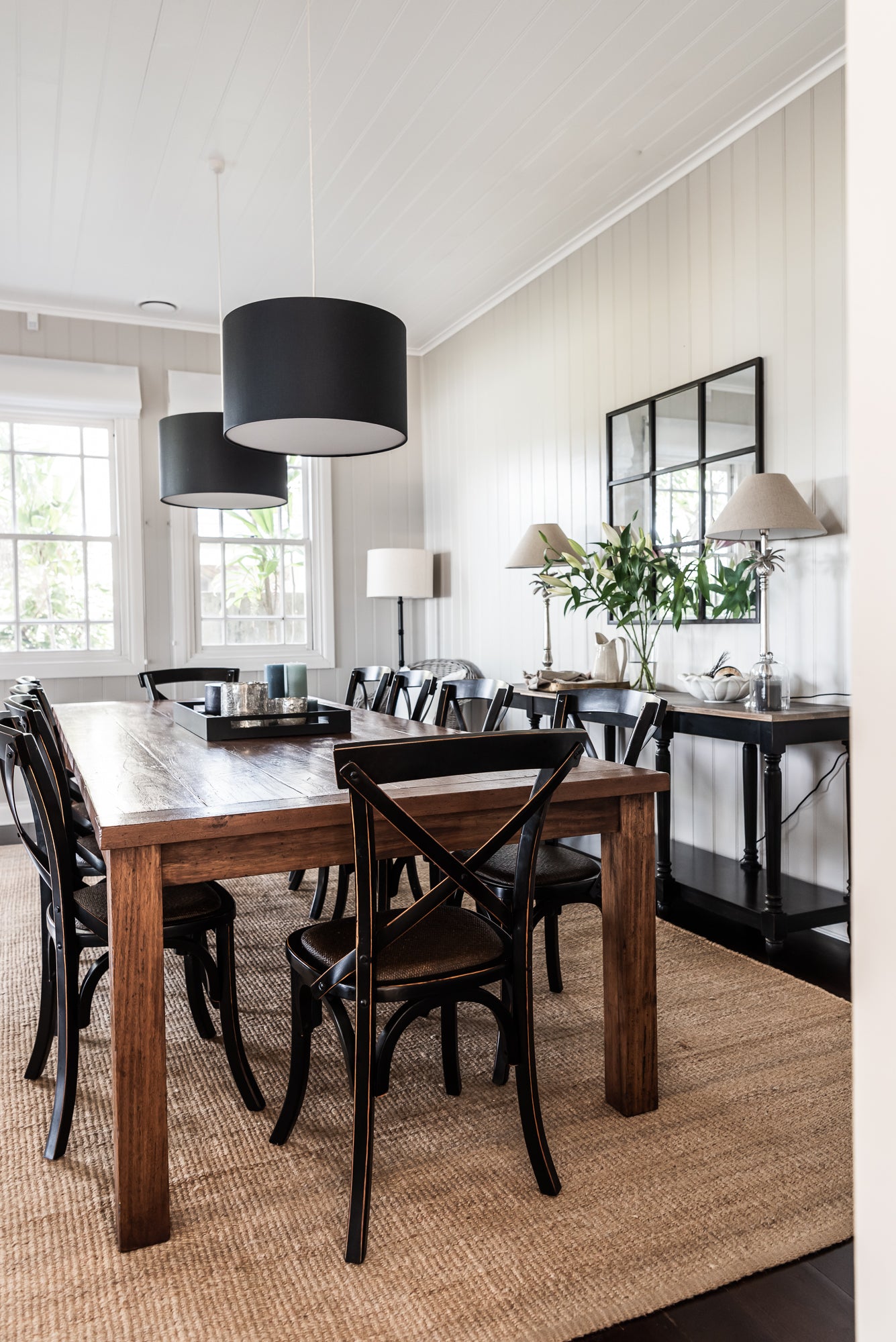 Dining room with wooden table and chairs, white walls, and large windows.