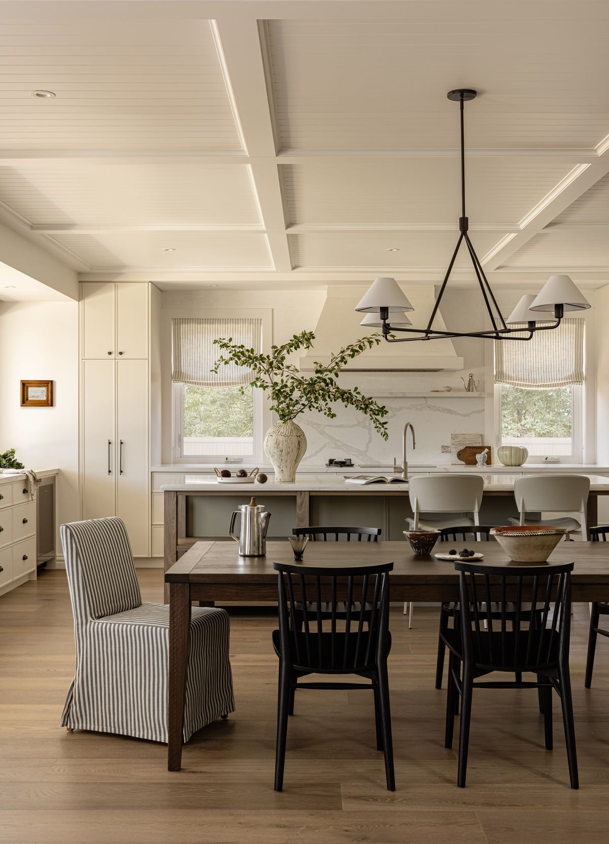 Modern kitchen with wooden dining table and chairs, white cabinets, and a chandelier.