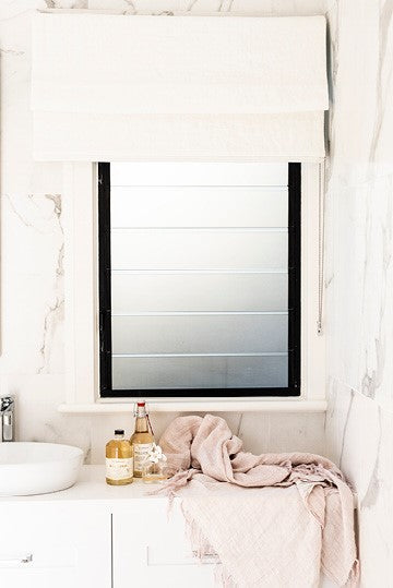 Elegant cream Roman shade in a marble bathroom interior with natural light filtering through the frosted window.