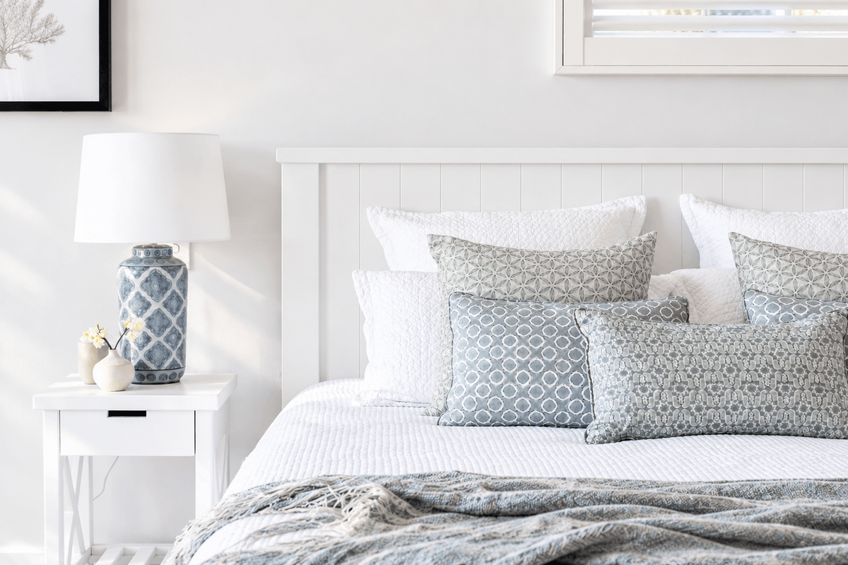 Alt text: White timber bed with coastal bedding and matching white bedside table.