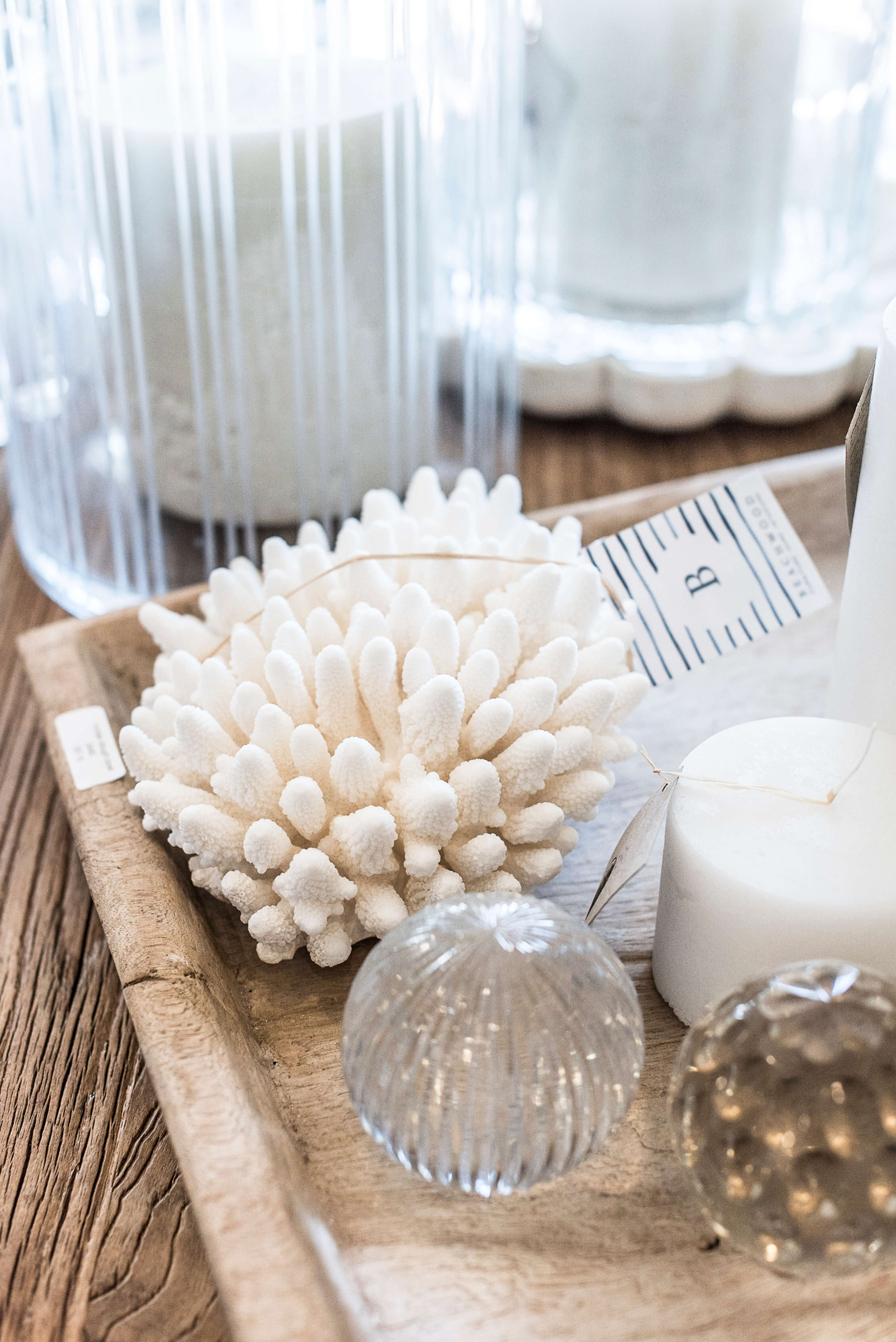 Artistic tabletop display featuring a white decorative coral piece, scented candle, and clear glass accents on a rustic wooden tray, perfect for a chic home decor inspiration