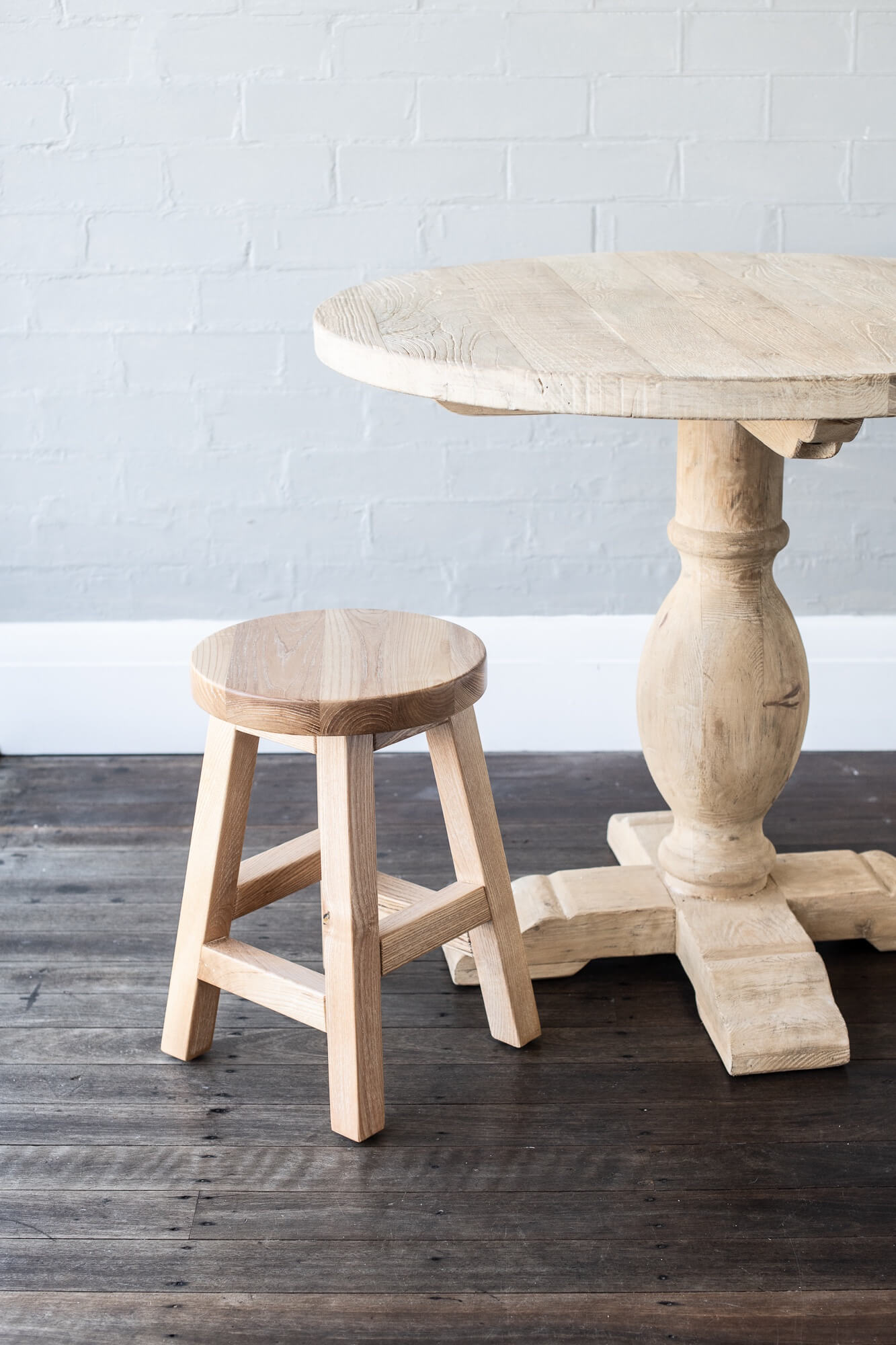Wooden elm table and stool against a light gray brick wall.
