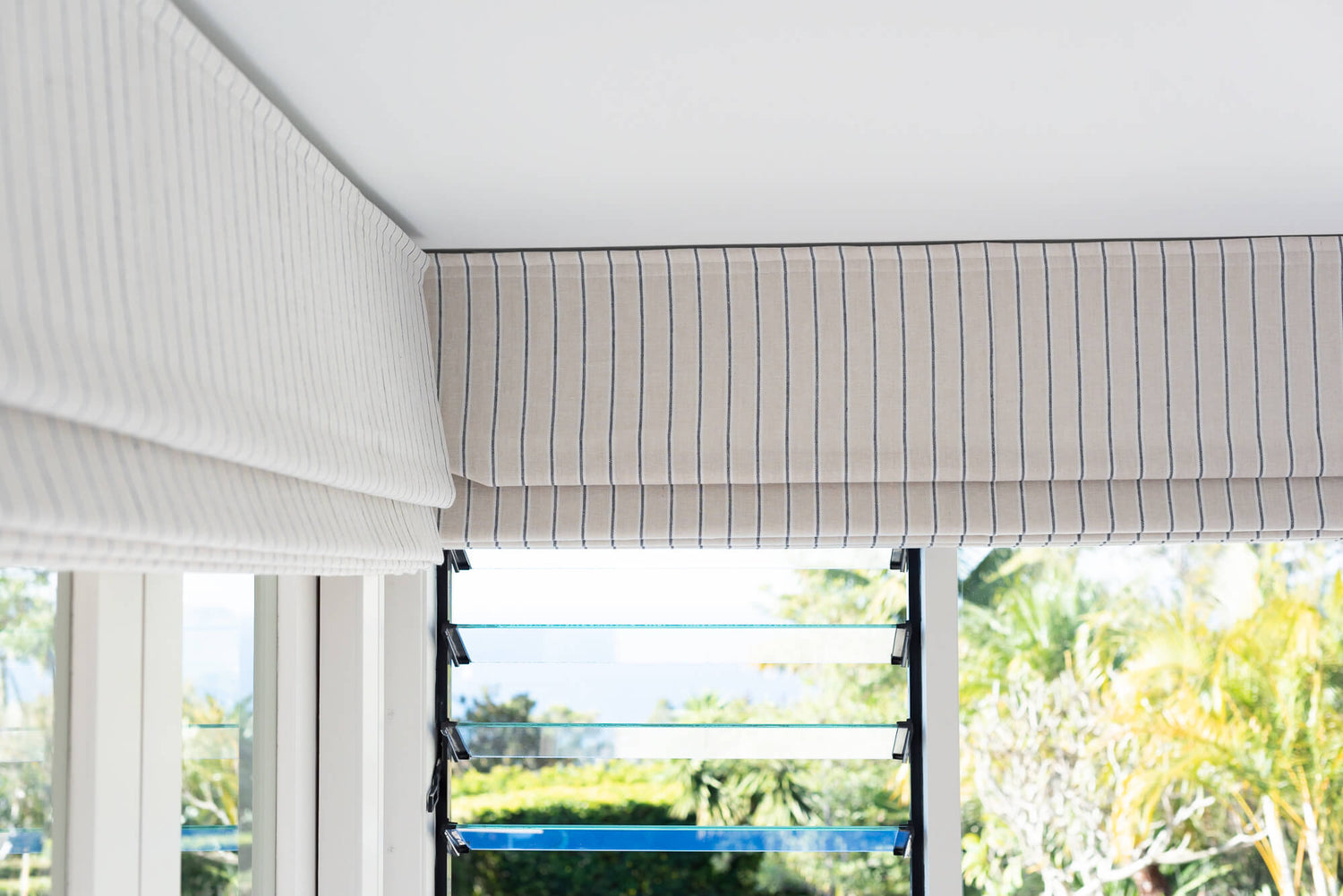 Striped Roman shade in a bright room with a view of a tropical pool area, offering a chic and airy window dressing.